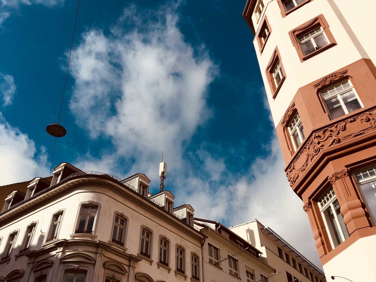 Blick nach oben in den blauen-weißen Himmel, 2 Altbauten ragen von unten in das Bild hinein.